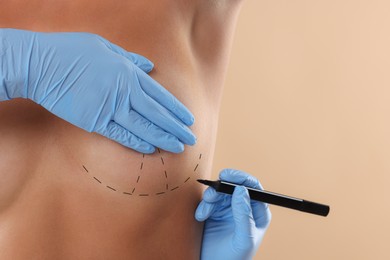 Breast augmentation. Doctor with marker preparing woman for plastic surgery operation against beige background, closeup. Space for text.