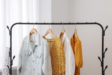 Photo of Rack with stylish women's clothes on hangers near light wall indoors