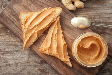 Photo of Jar with creamy peanut butter and toasts on wooden board