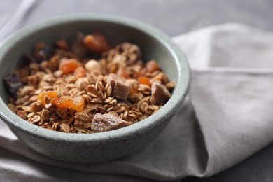 Photo of Tasty granola in bowl and napkin on gray table, closeup