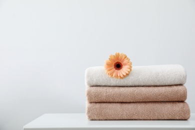 Stack of fresh towels with flower on table against white background. Space for text