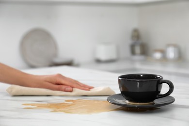 Photo of Woman cleaning spilled coffee on white marble table in kitchen, closeup. Space for text
