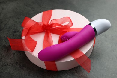 Photo of Gift box and pink vaginal vibrator on grey table. Sex toy