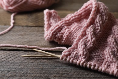 Photo of Pink knitting and needles on wooden table, closeup