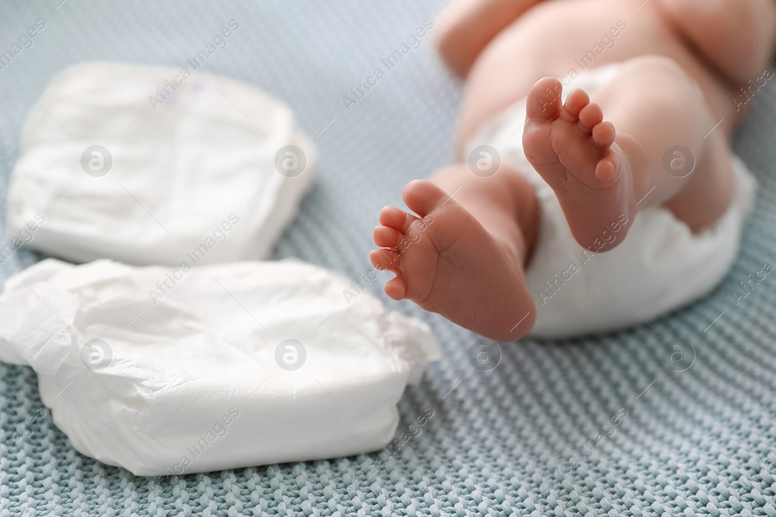 Photo of Cute little baby in diaper lying on bed, closeup