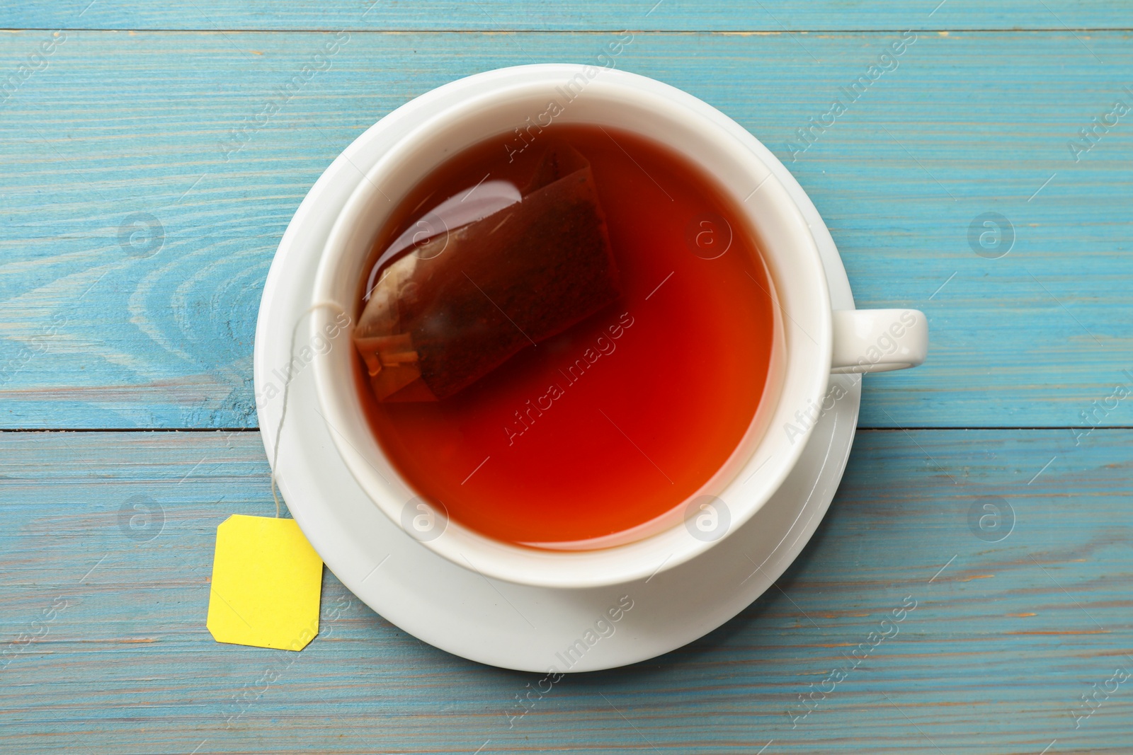 Photo of Tea bag in cup with hot drink on light blue wooden table, top view