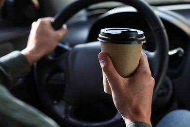 Photo of Coffee to go. Man with paper cup of drink driving his car, closeup