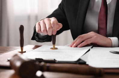 Photo of Notary stamping document at table in office, closeup