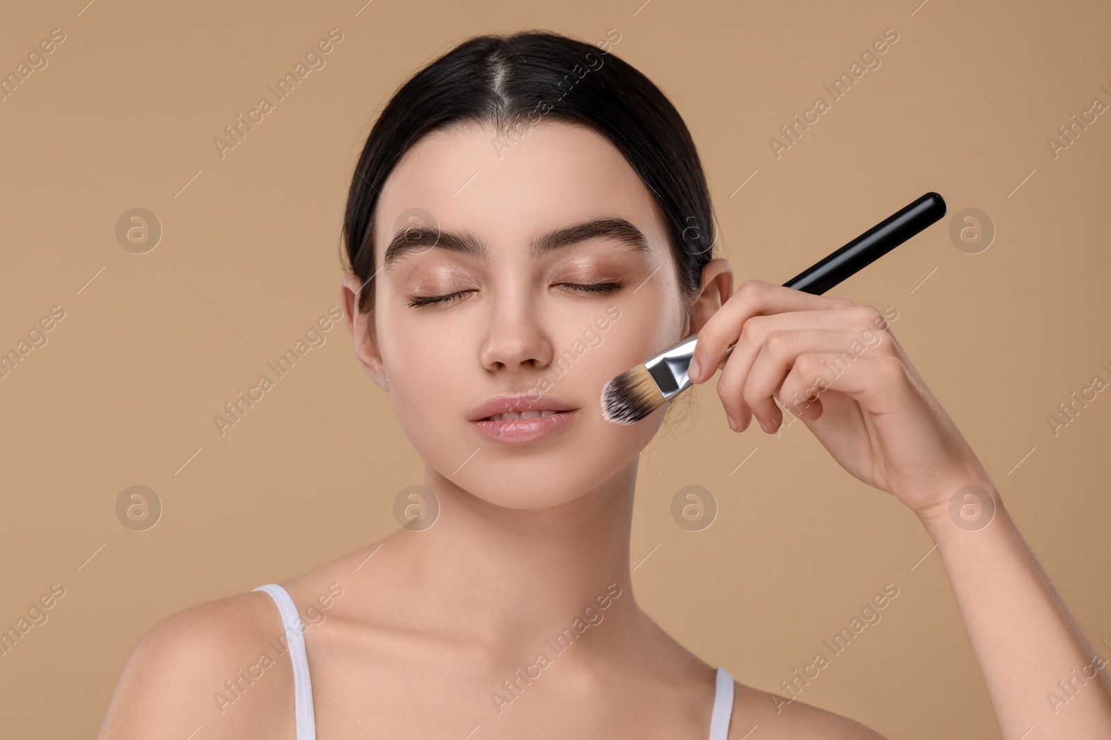 Photo of Teenage girl with makeup brush on beige background