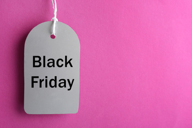 Photo of Blank tag hanging on violet background, space for text. Black Friday concept