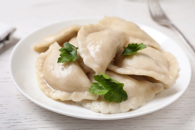 Photo of Plate of tasty cooked dumplings served on white wooden table, closeup
