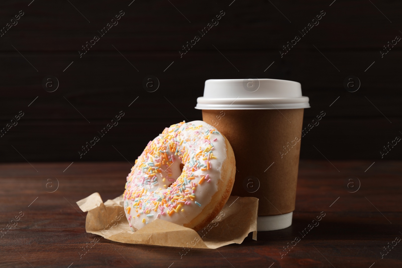 Photo of Yummy donut and paper cup on wooden table against brown background