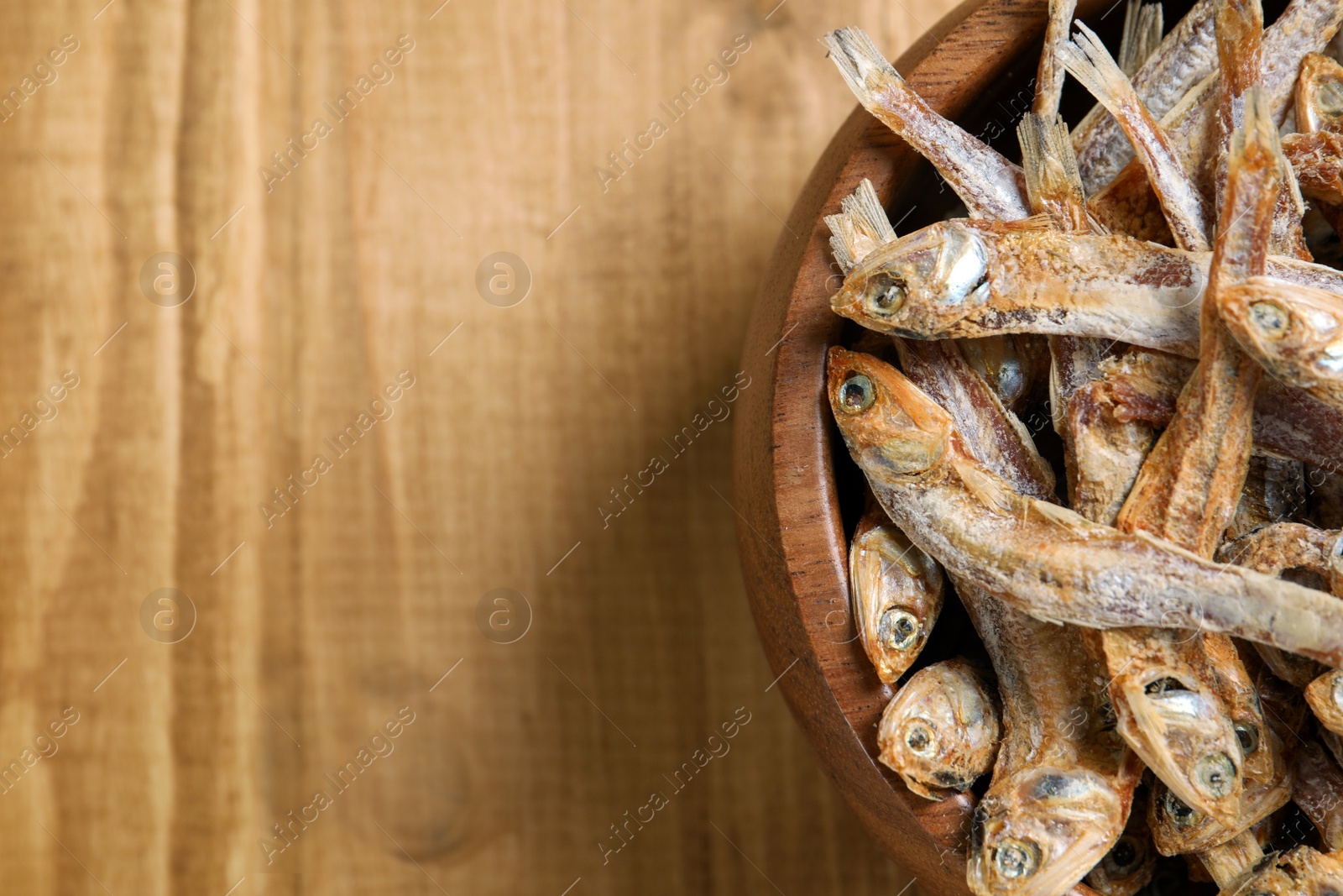 Photo of Bowl of tasty dried anchovies on wooden table, top view. Space for text