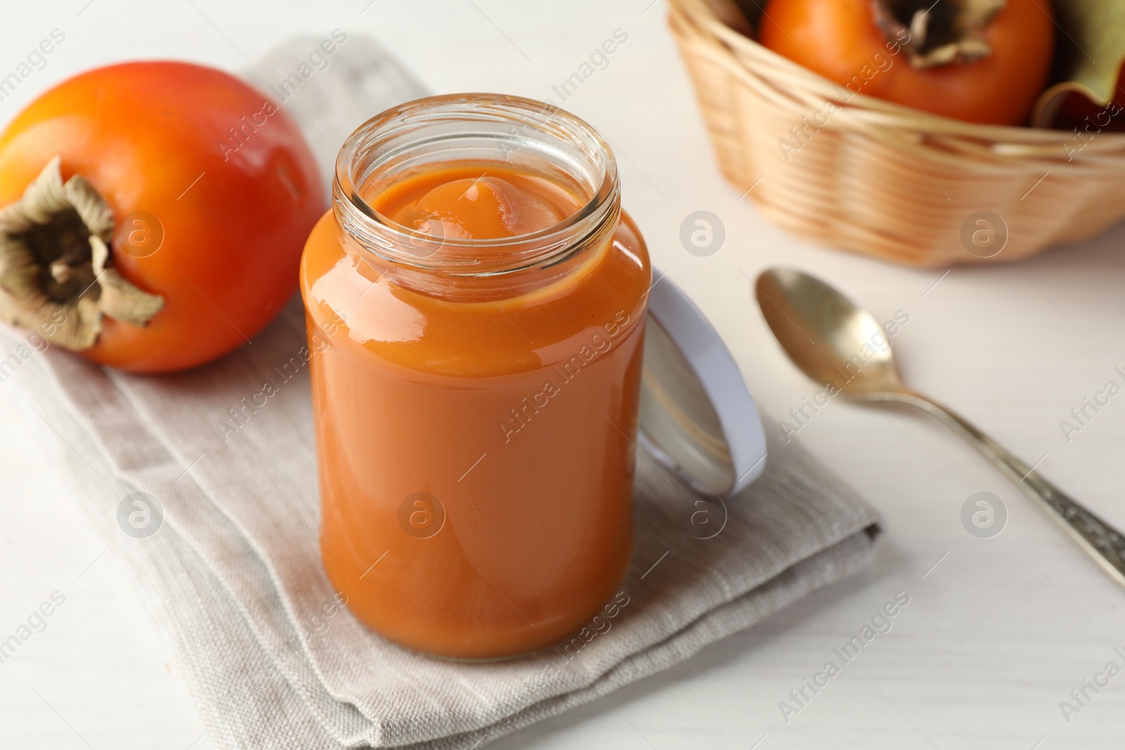 Photo of Delicious persimmon jam in glass jar served on white wooden table, closeup