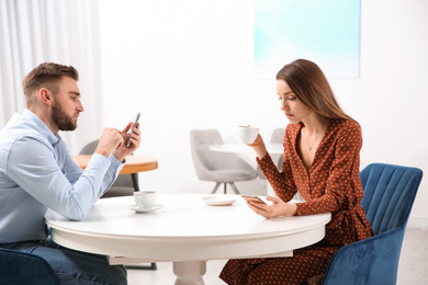 Photo of Couple addicted to smartphones ignoring each other in cafe. Relationship problems