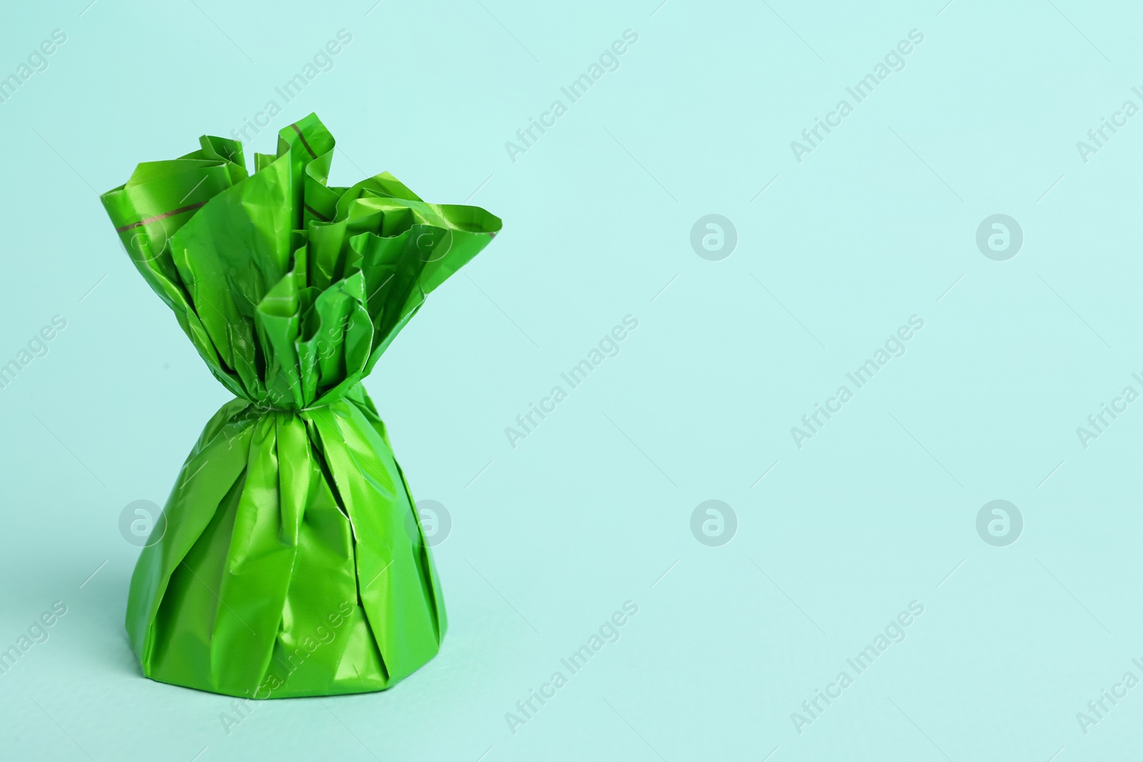 Photo of Candy in green wrapper on light blue background. Space for text