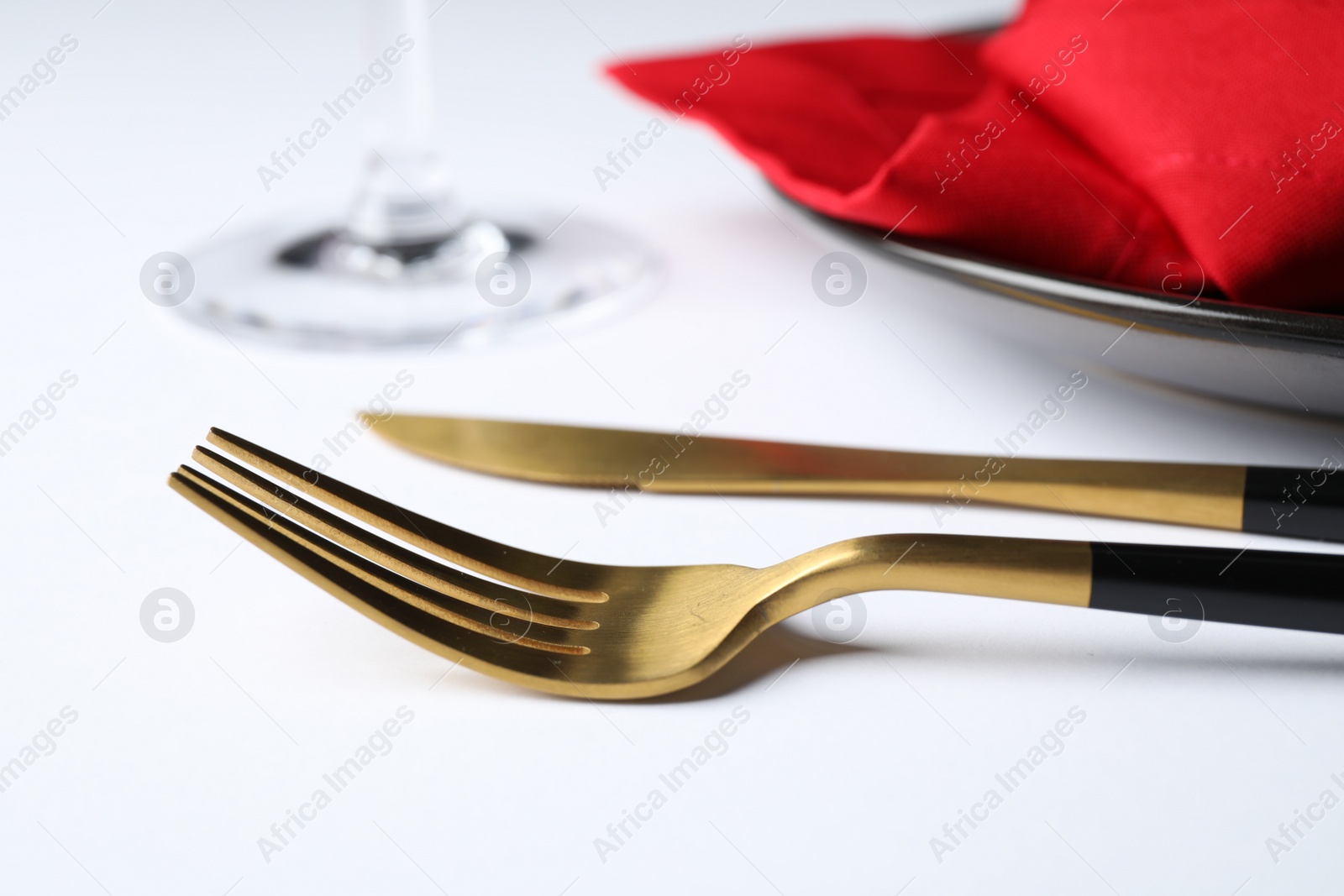 Photo of Golden cutlery near plate on white table, closeup