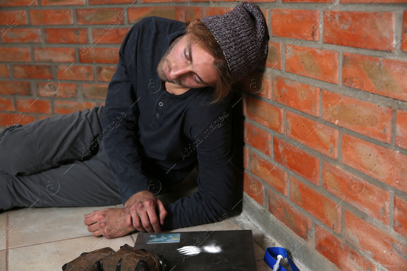 Photo of Young addicted man sitting near brick wall after using drugs