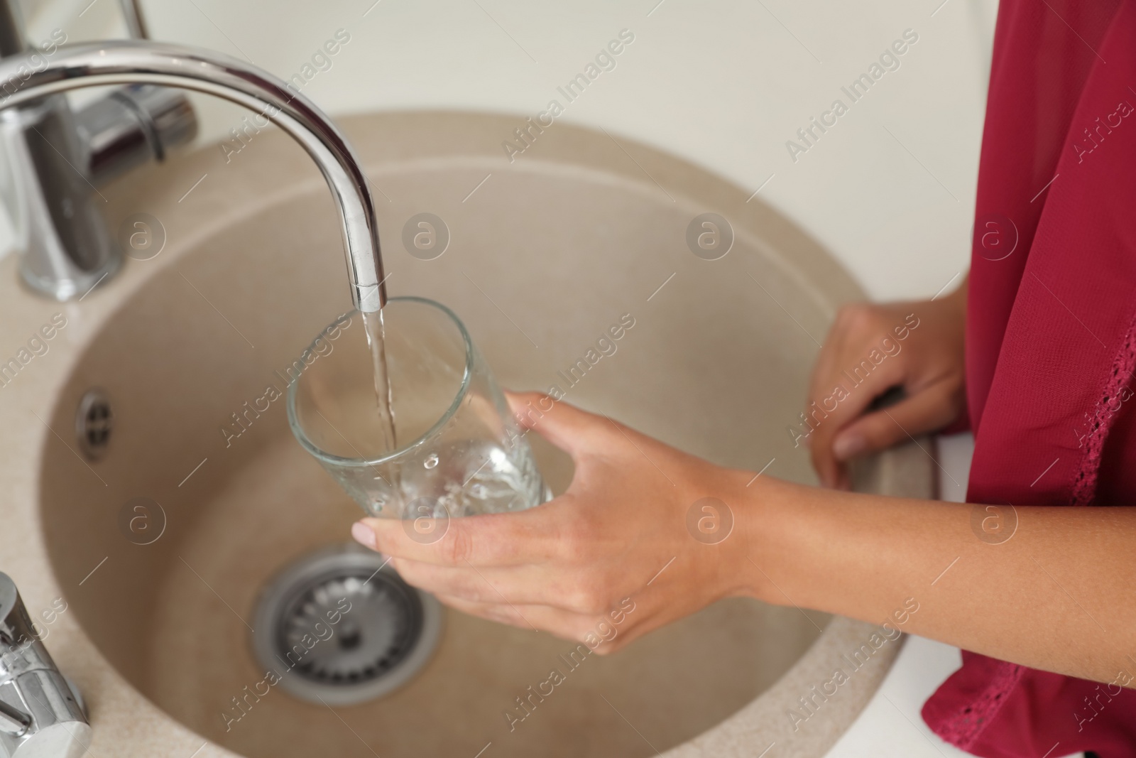 Photo of Woman pouring water into glass in kitchen, closeup