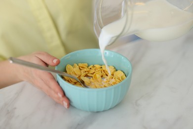 Making breakfast. Woman pouring milk from jug into bowl with cornflakes at white marble table, closeup