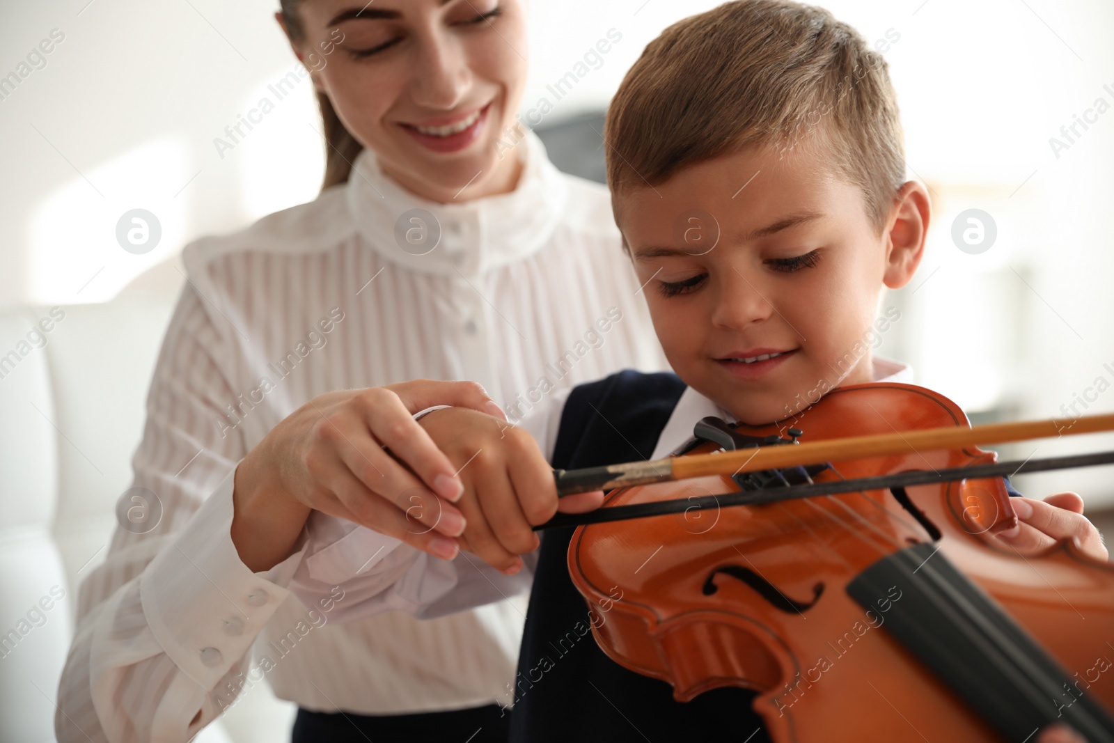 Photo of Young woman teaching little boy to play violin indoors