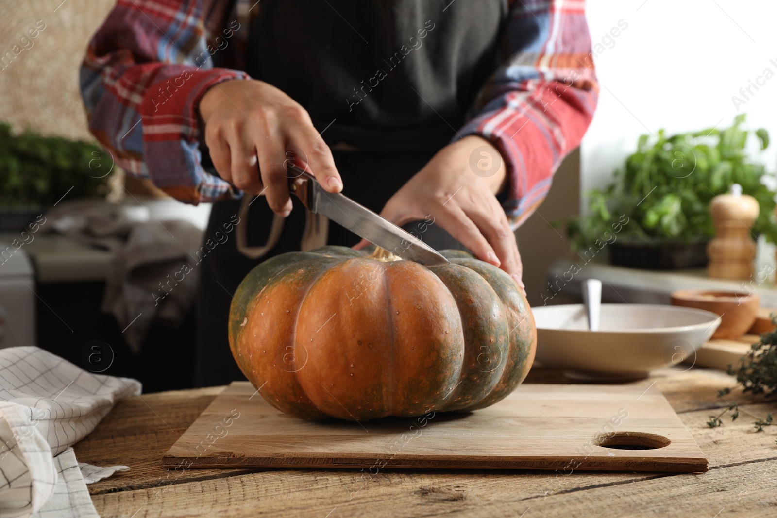 Photo of Woman cutting fresh ripe pumpkin at wooden table in kitchen, closeup