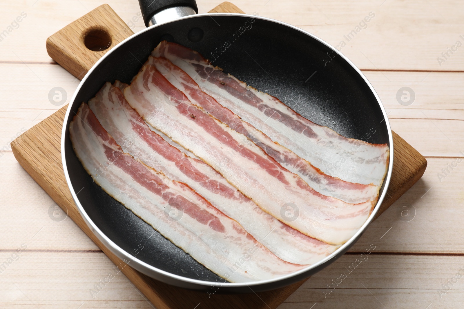 Photo of Slices of raw bacon in frying pan on wooden table, closeup