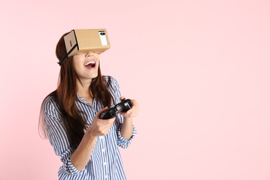 Photo of Young woman using cardboard virtual reality headset on color background. Space for text