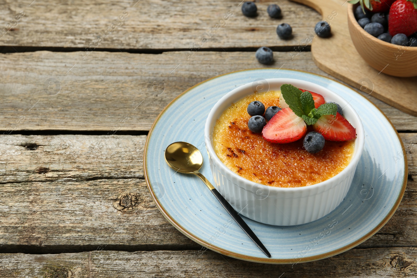 Photo of Delicious creme brulee with berries and mint in bowl on wooden table. Space for text