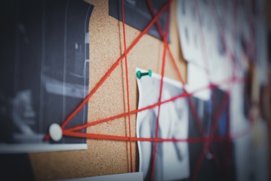 Detective board with crime scene photos and red threads, closeup