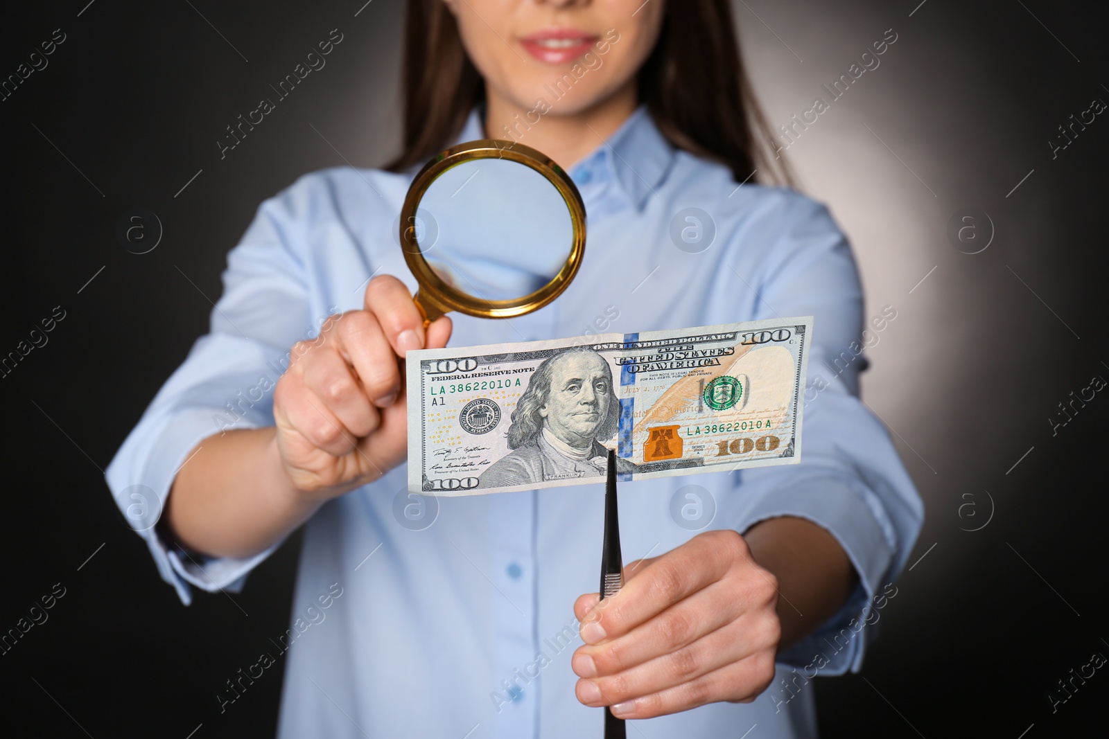 Photo of Expert authenticating 100 dollar banknote with magnifying glass against dark background, closeup. Fake money concept