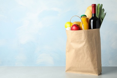 Photo of Paper bag with groceries on grey table against light blue background. Space for text