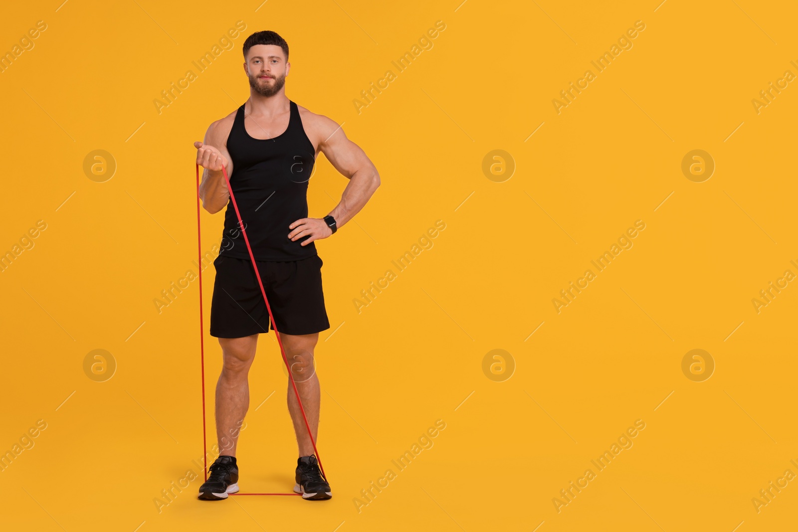 Photo of Young man exercising with elastic resistance band on orange background. Space for text