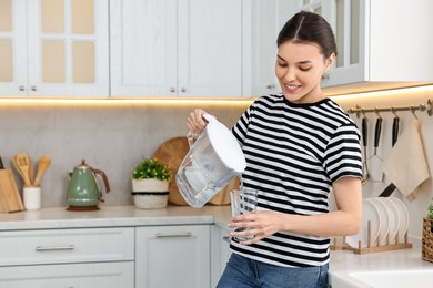 Photo of Woman pouring water from filter jug into glass in kitchen