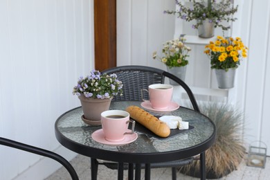 Photo of Cups of coffee, potted plant, bread and cheese on glass table. Relaxing place at outdoor terrace