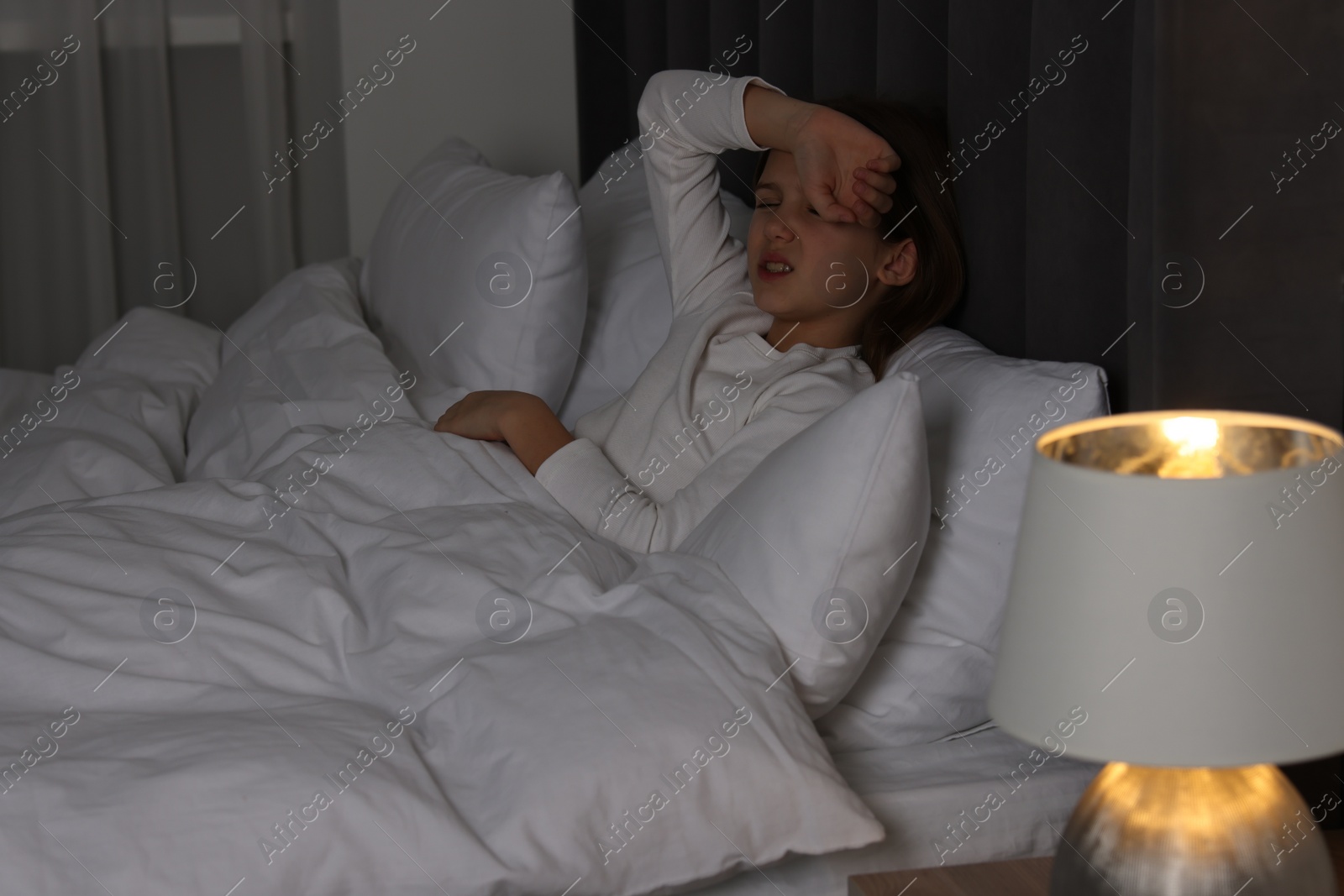 Photo of Little girl suffering from headache in bed at night