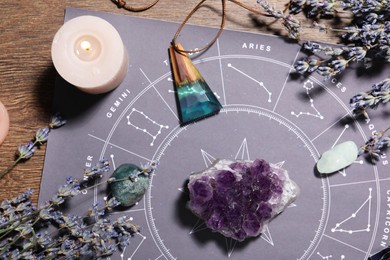 Photo of Astrology prediction. Zodiac wheel, gemstones, burning candle and lavender on wooden table, flat lay