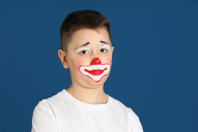 Photo of Preteen boy with clown makeup on blue background, space for text. April fool's day