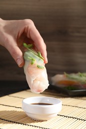 Photo of Woman dipping delicious spring roll into soy sauce at table, closeup