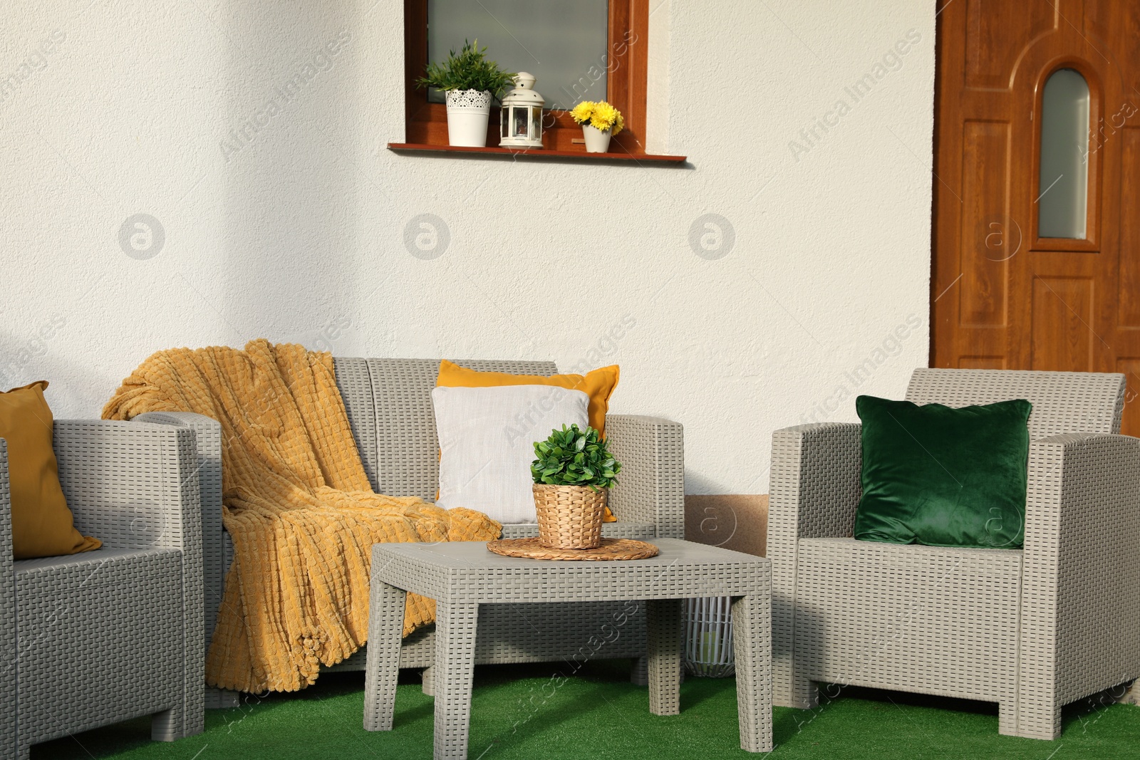 Photo of Beautiful rattan garden furniture, soft pillows, blanket and houseplant near white wall