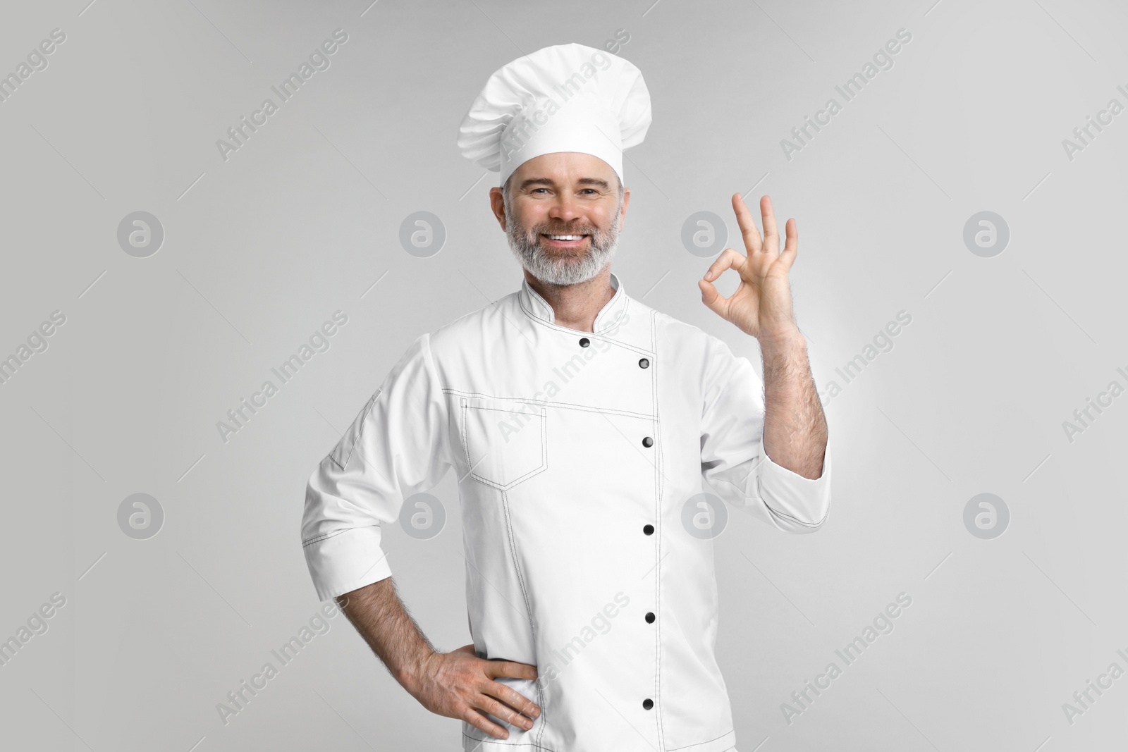 Photo of Happy chef in uniform showing OK gesture on grey background