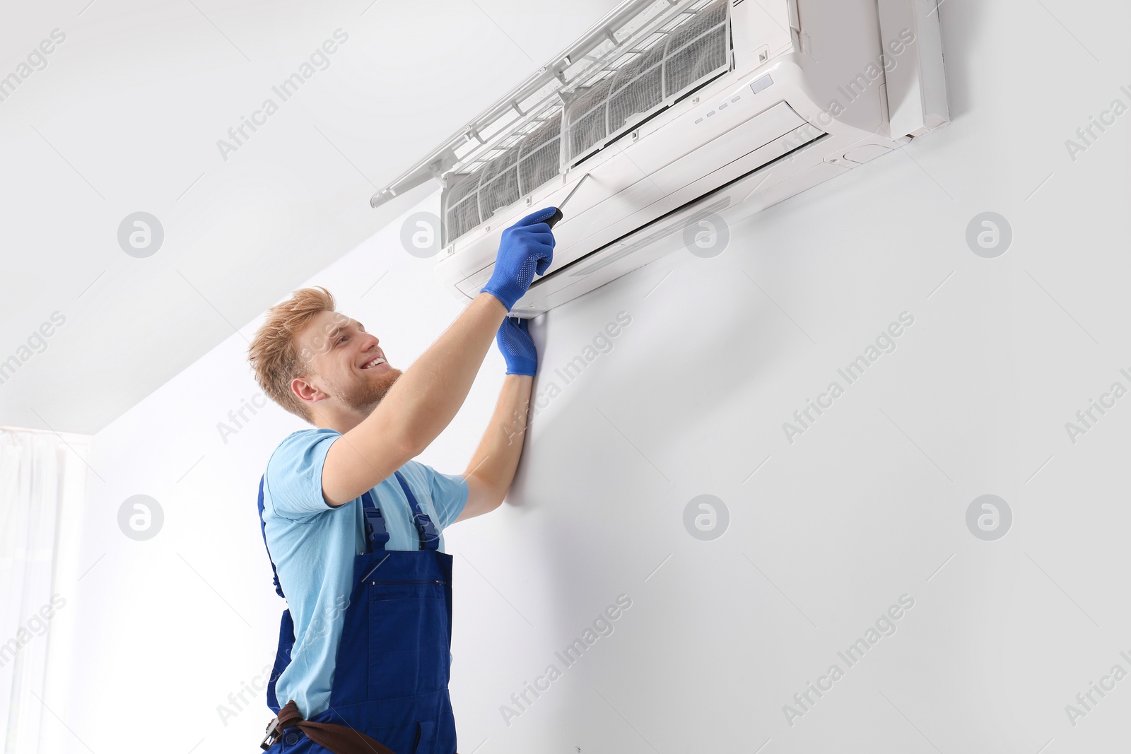 Photo of Professional technician maintaining modern air conditioner indoors