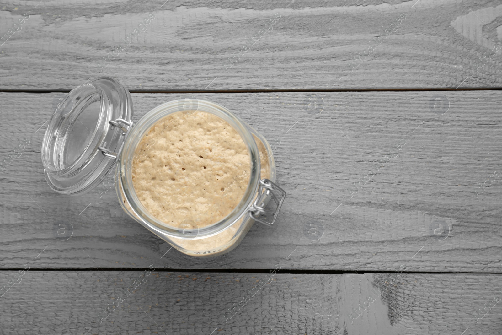 Photo of Leaven in glass jar on grey wooden table, top view. Space for text