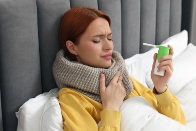 Photo of Young woman with scarf holding throat spray in bed