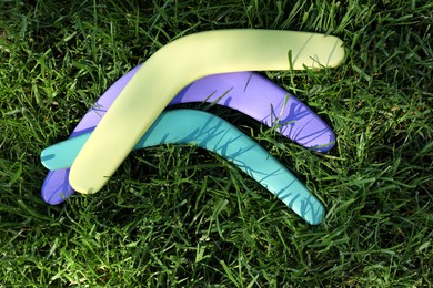 Violet, yellow and turquoise wooden boomerangs on green grass outdoors, above view