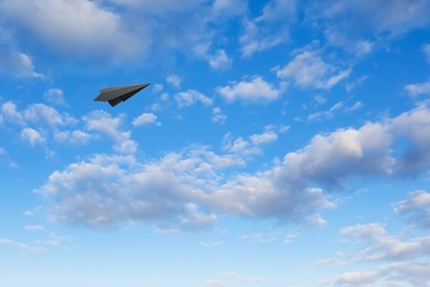 Image of Black paper plane flying in blue sky with clouds