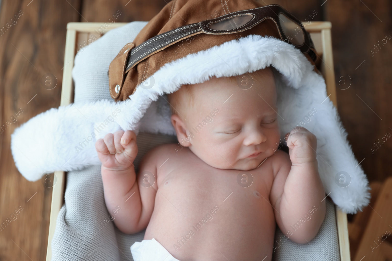 Photo of Cute newborn baby wearing aviator hat in wooden crate, top view