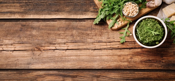 Image of Bowl of tasty arugula pesto and ingredients on wooden table, flat lay with space for text. Banner design