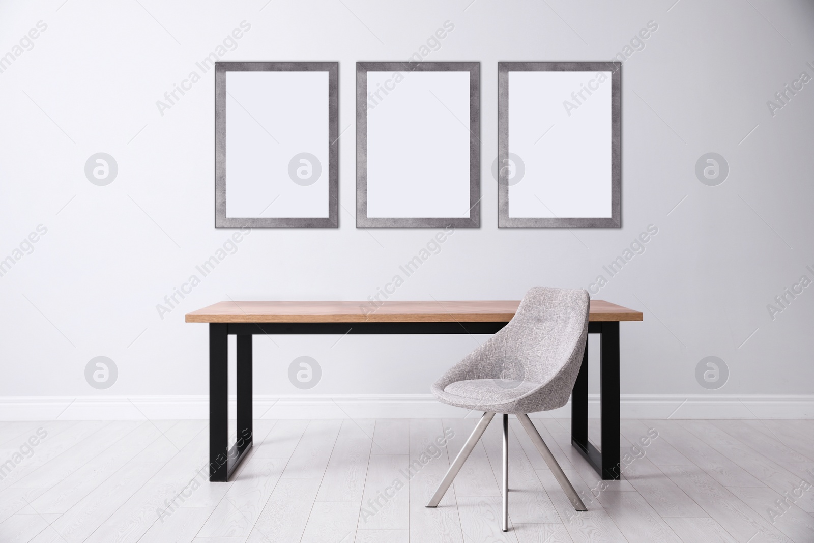 Image of Table and chair near light wall with empty posters. Mockup for design