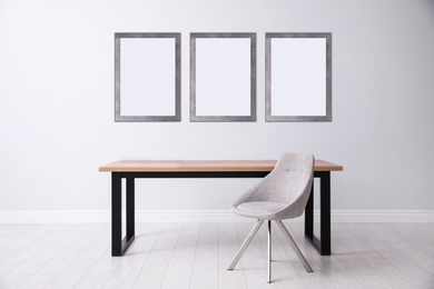 Image of Table and chair near light wall with empty posters. Mockup for design